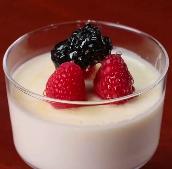 Small glass cup filled with creamy panna cotta and topped with raspberries and blackberries