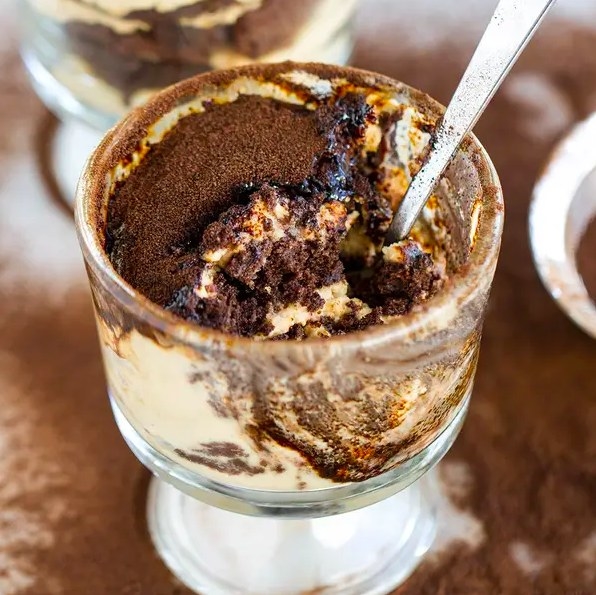 Tiny glass parfait cup containing brownie tiramisu with a metal spoon