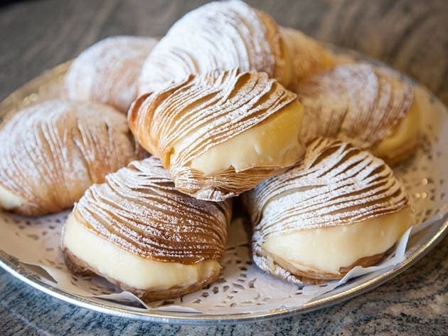 Eight sfogliatella sit on a white plate; cream bursts out of each of them