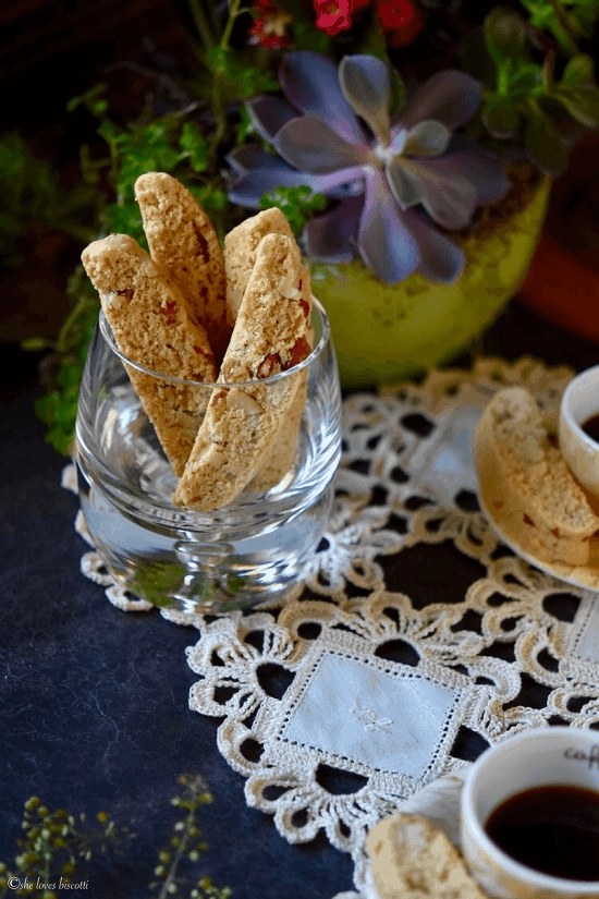 A glass cup holds four crumbly-looking, almond biscotti