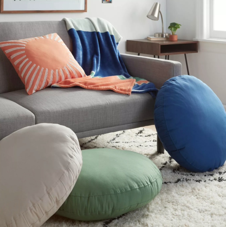 Large round pillows in blue, gray, and green sitting on a floor next to a couch