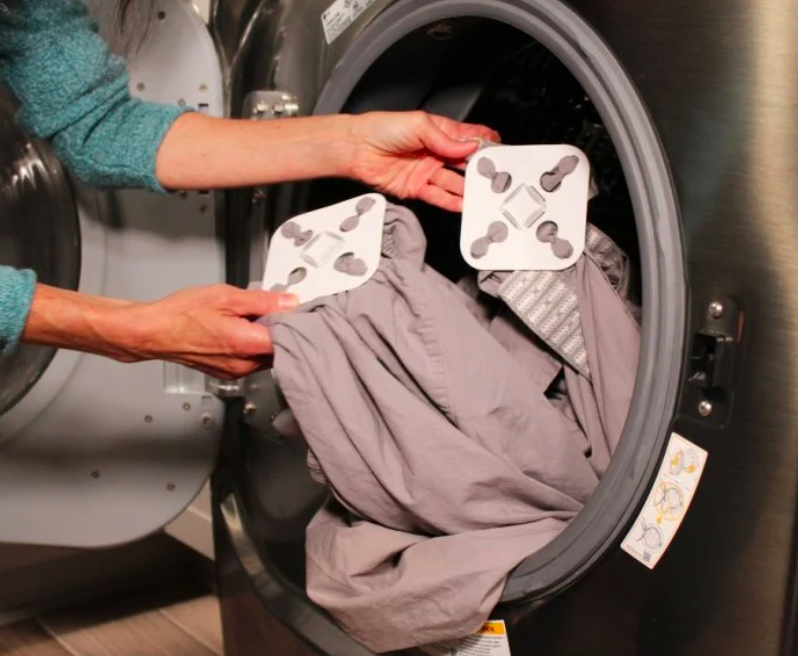 A person pulling their sheets out of the dryer with the detanglers attached