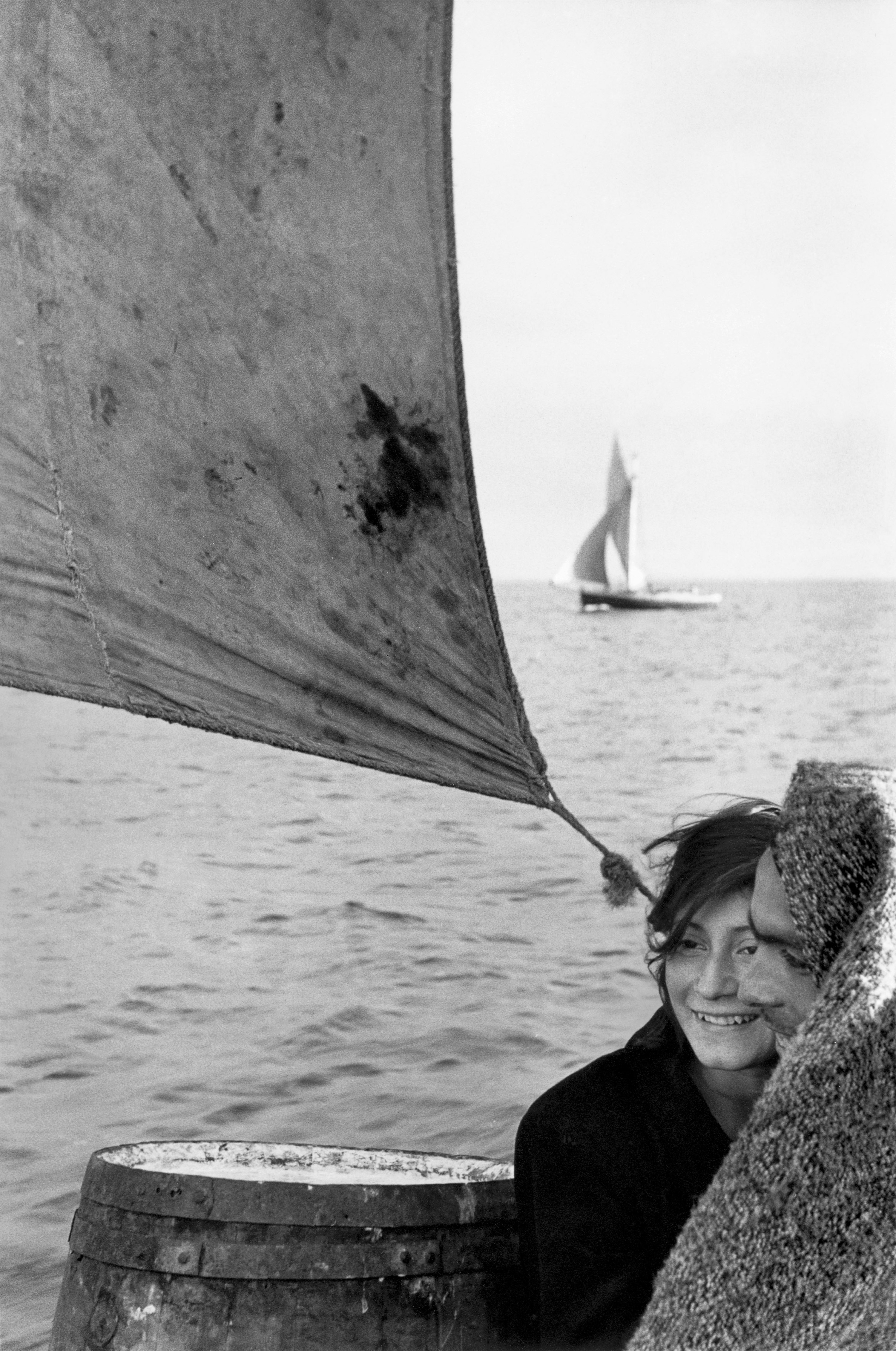 A young couple on a boat, with a sail above them and the woman smiling