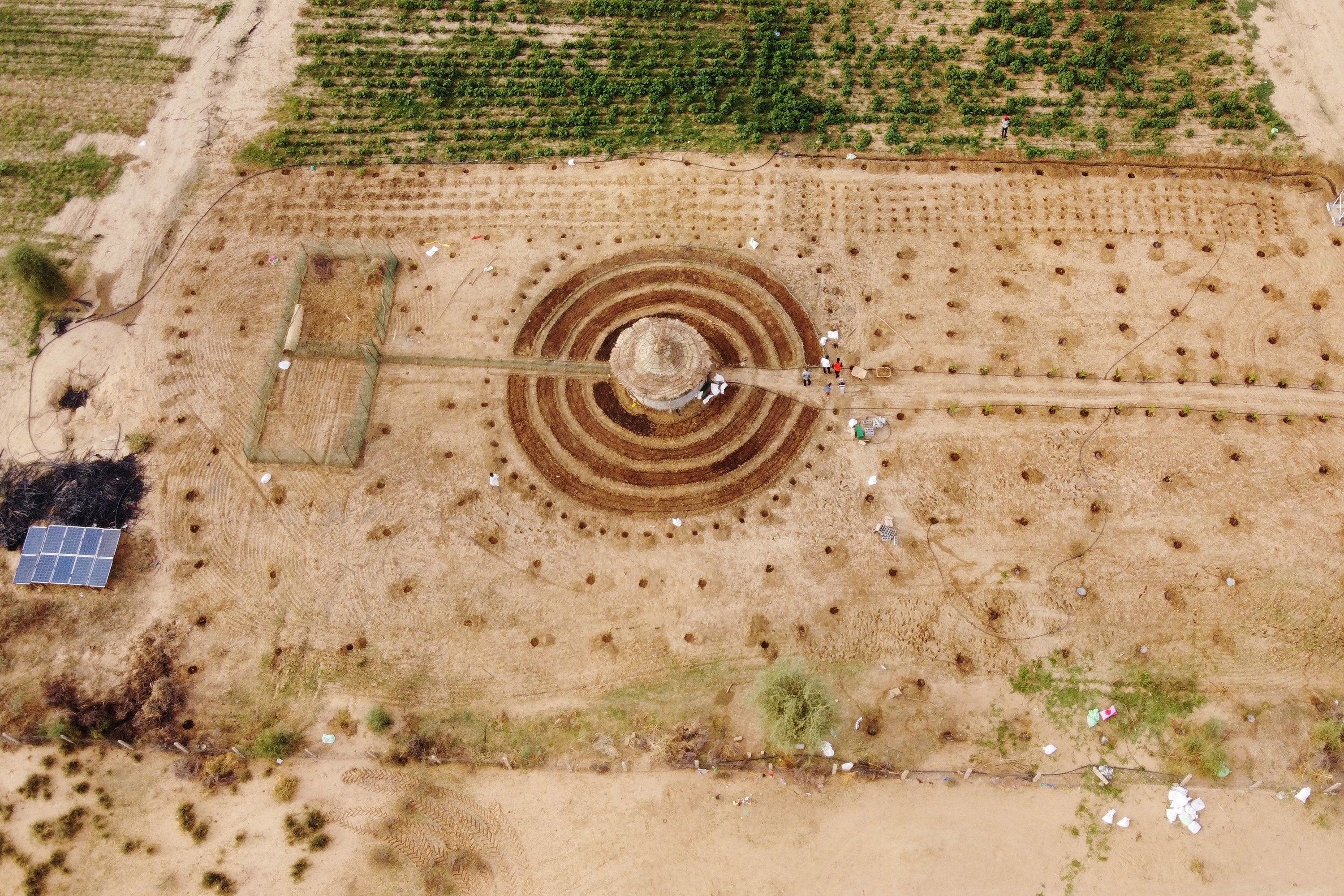 An overhead shot of a large series of circles carved into farmland, with people and solar panels nearby