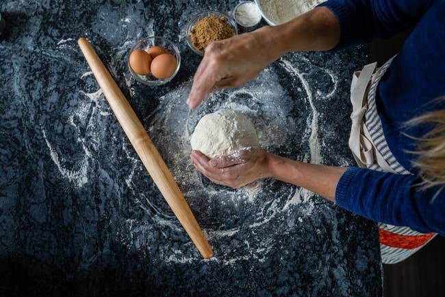Long wooden rolling pin on marble table with pasta ingredients out