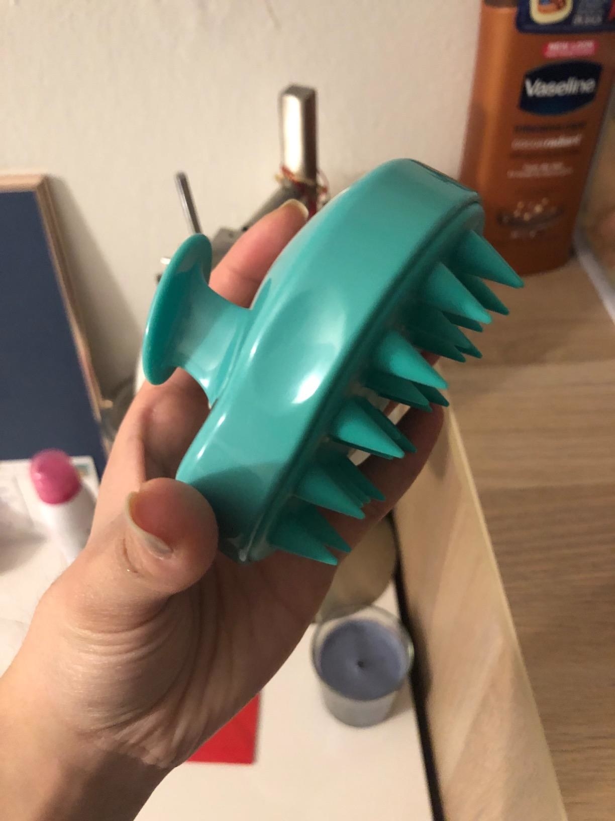 image of the light green scalp massager in between reviewer&#x27;s fingers