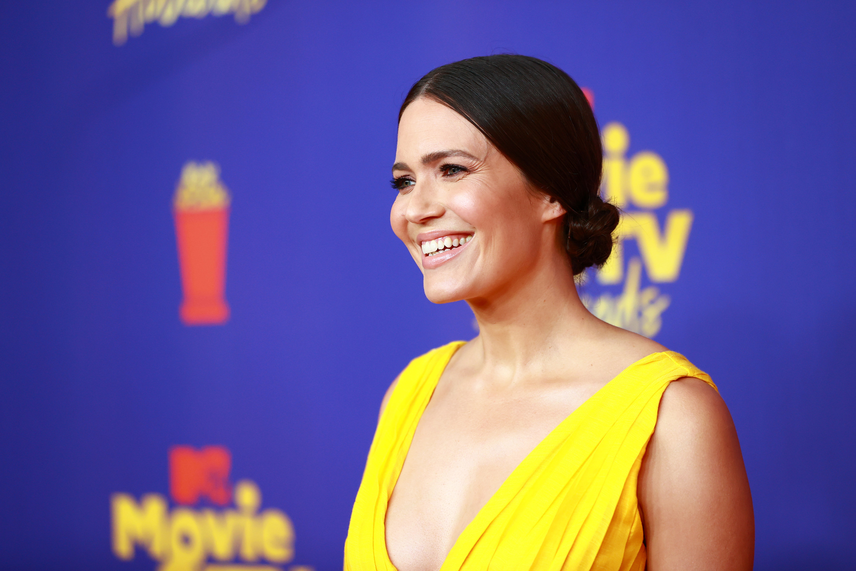 Photo of Mandy Moore in a bright yellow dress smiling at something off-camera