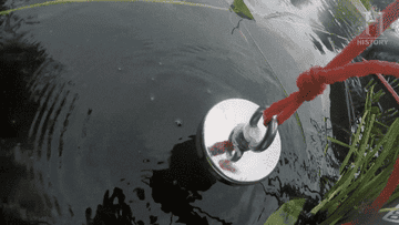 a man lowering a rope with a magnet on the end into a lake