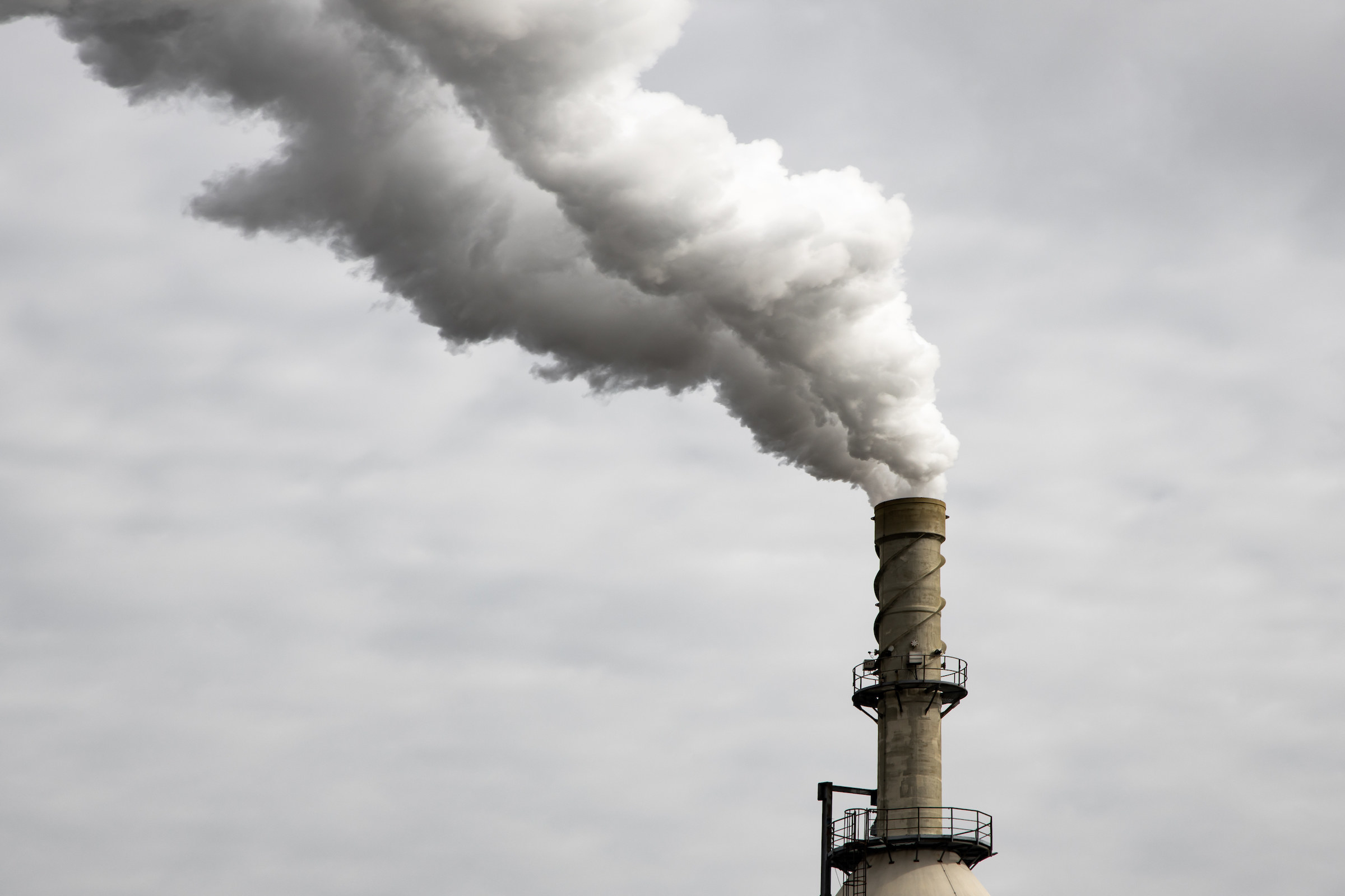 A factory chimney spewing smoke into a grey sky