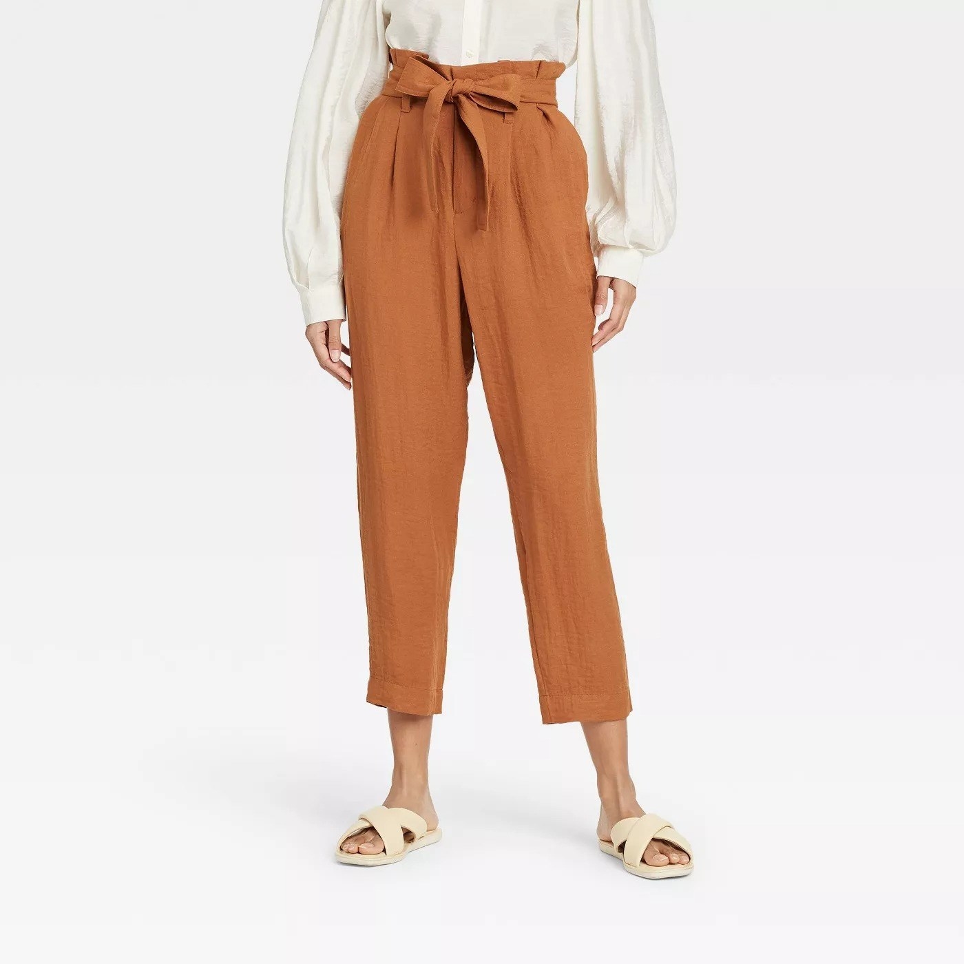 Model wearing camel high waisted pants with a tie waist, stops at the ankle