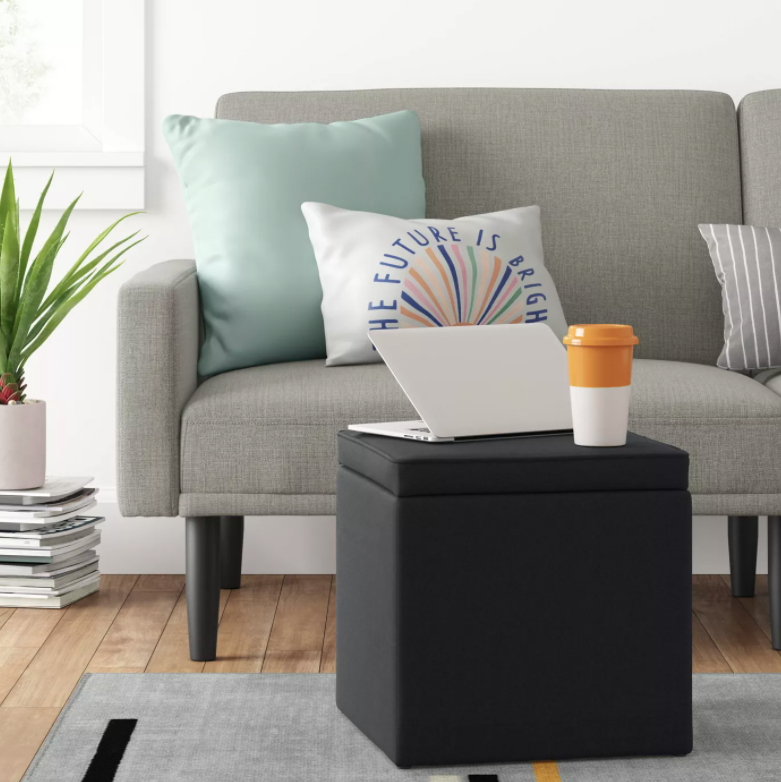 Storage ottoman in black with a laptop and cup on top