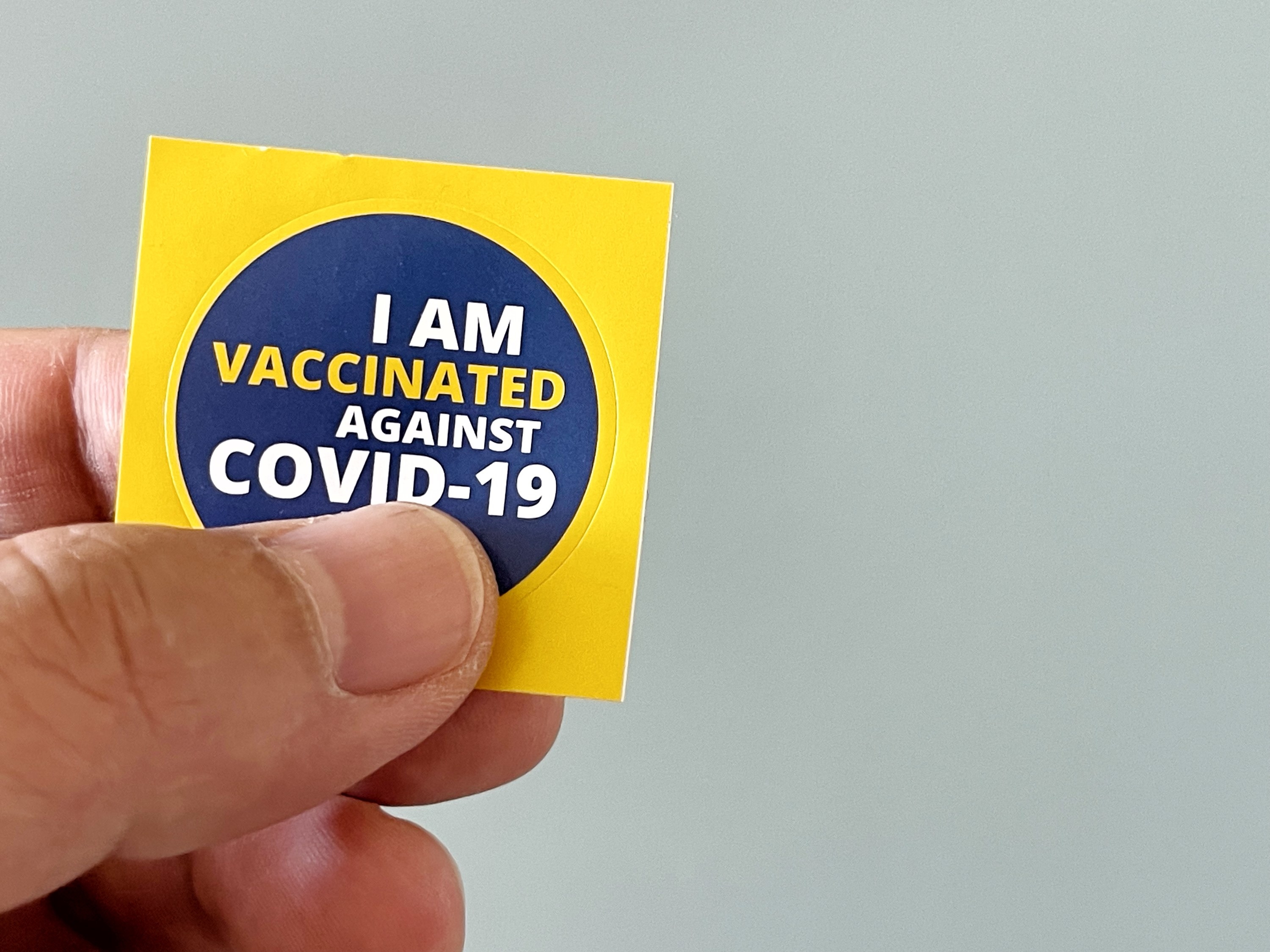 Man holding a sticker that says, &quot;I Am Vaccinated Against COVID-19&quot;