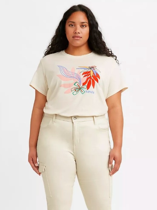 Model wearing the scoop-neck cream colored shirt. Multi-colored floral design on the center of the T-shirt