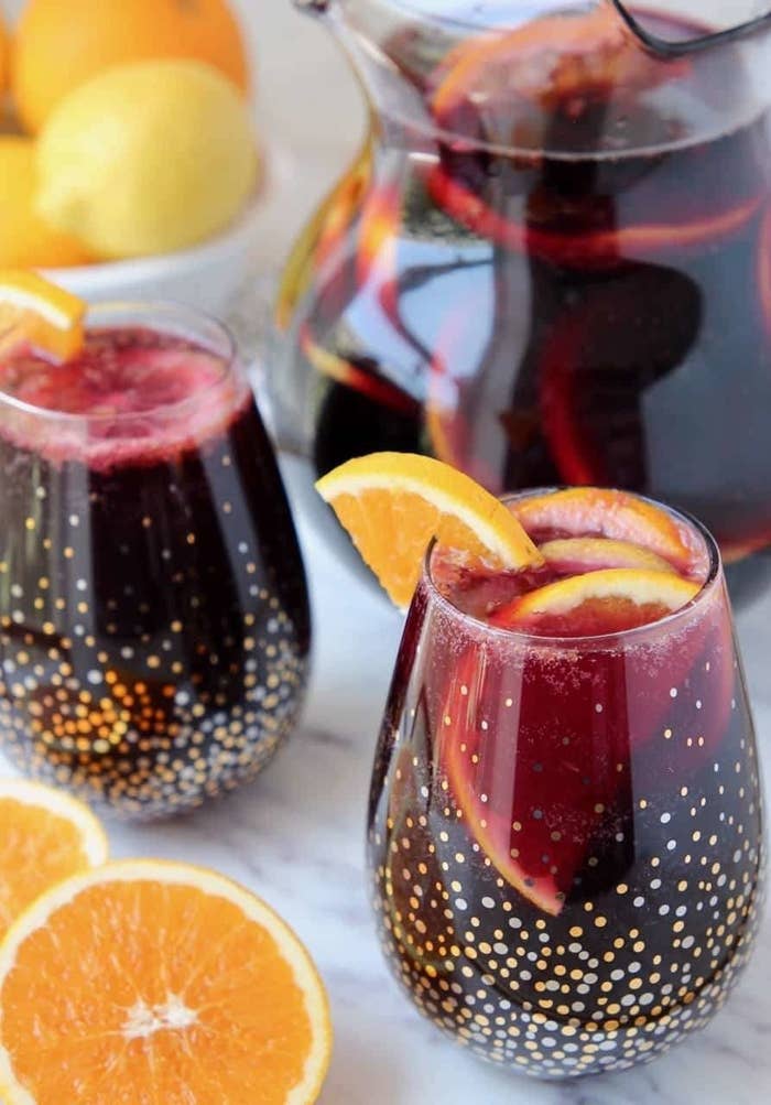 Red sangria in stemless wine glasses garnished with oranges. 