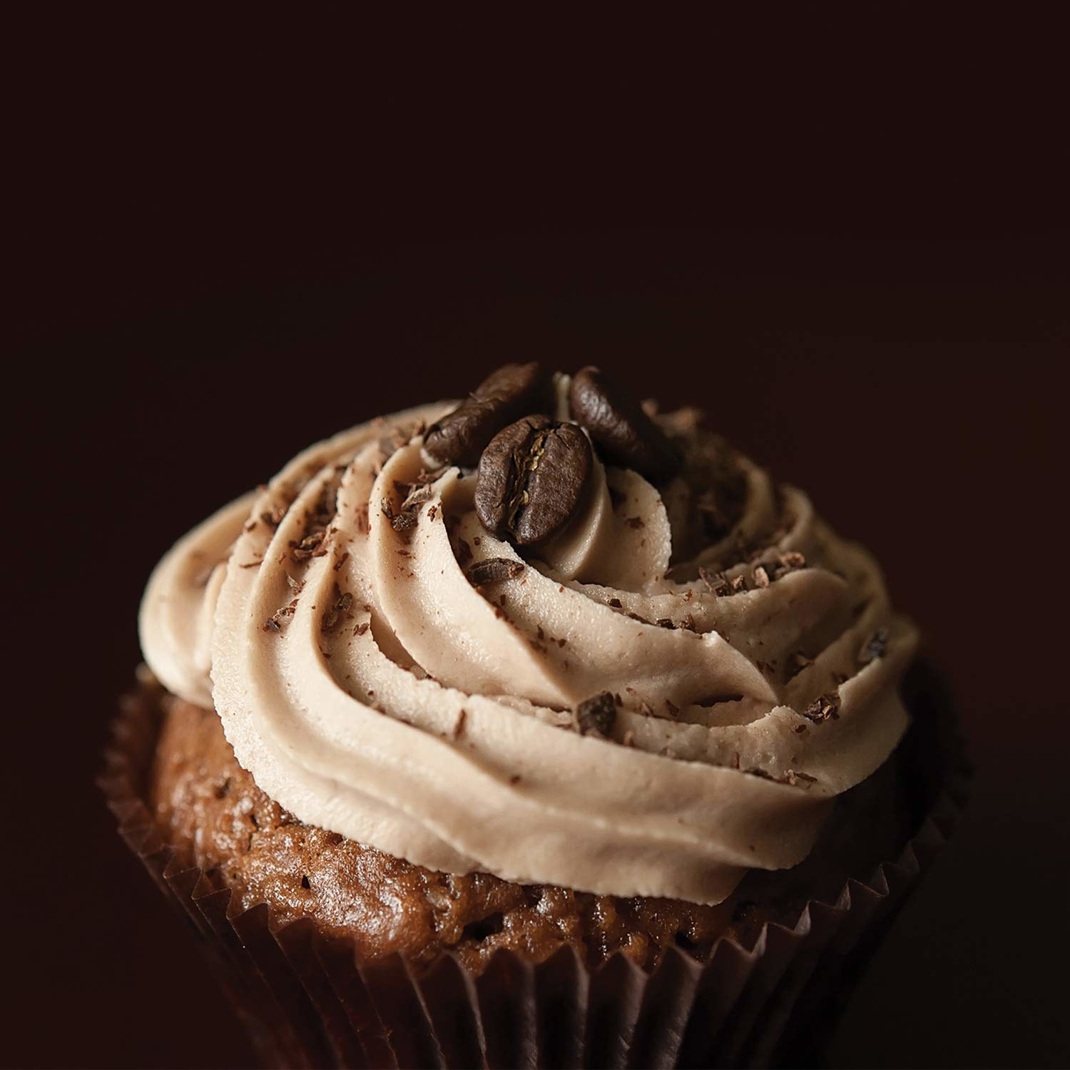 A cupcake with icing on it and two coffee beans on top.