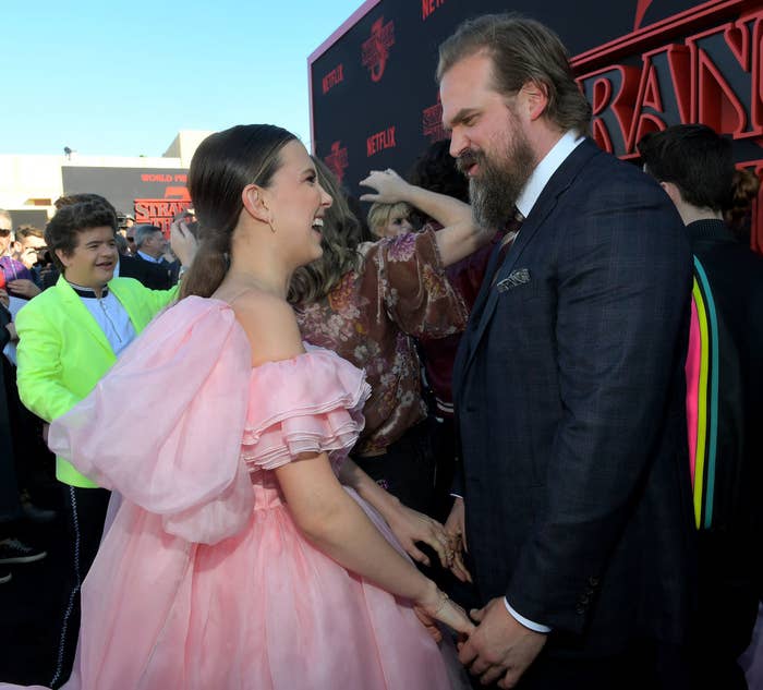 Millie Bobby Brown (L) and David Harbour holding hands and smiling at each other at the "Stranger Things" Season 3 World Premiere