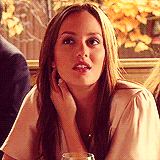 A close-up of Blair Waldorf giving someone offscreen a grimacing smile and halfhearted wave