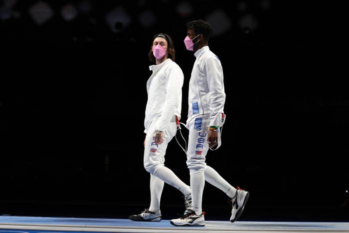 Two outfitted fencers walk side by side and wear matching face masks