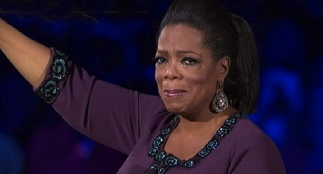 Oprah crying with one arm raised