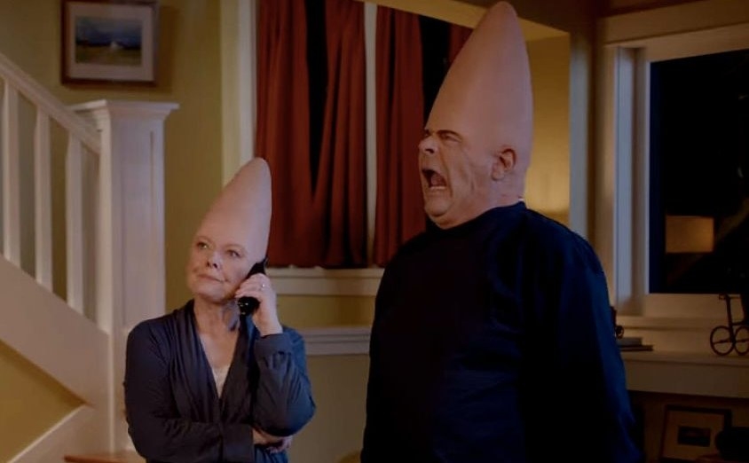 The &quot;coneheads&quot;, Mary Margaret and Donald stand in their living room, Mary Margaret is on the phone while Donald pulls a face.