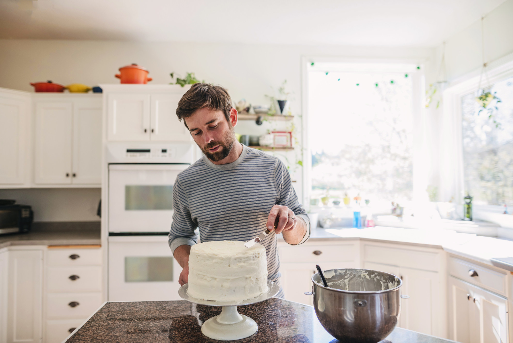 A person icing a cake in their kitchen