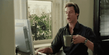 jim carry from a scene in bruce almighty drinking coffee with one hand and typing with the other
