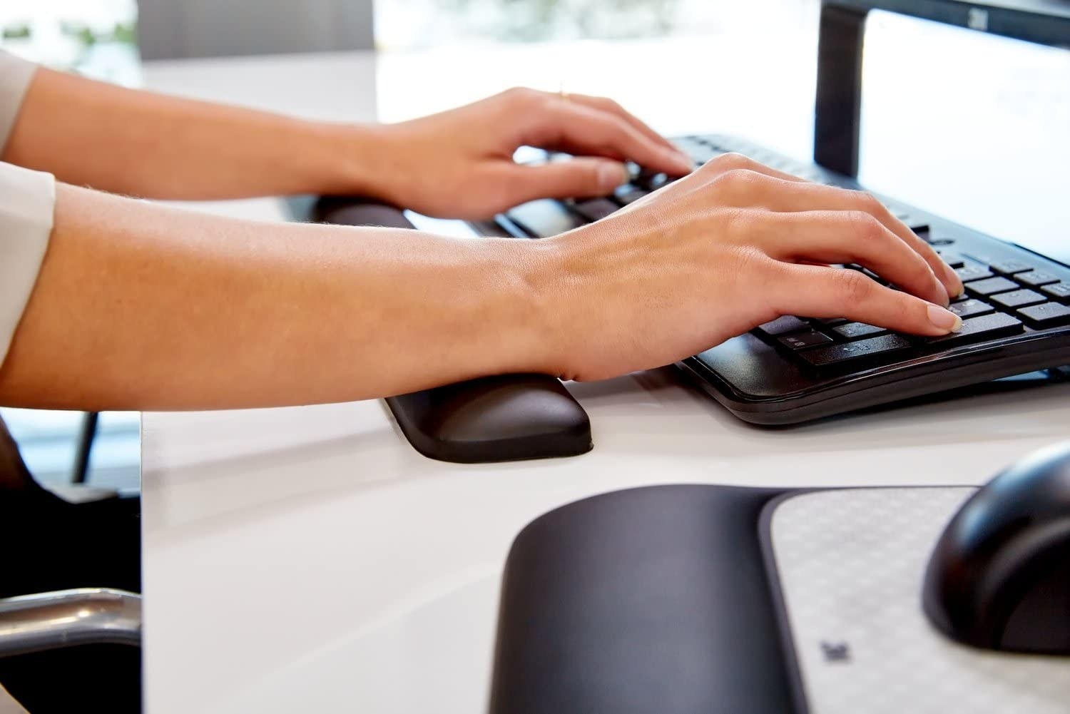A person typing on their laptop with a long fabric wrist rest underneath their arms