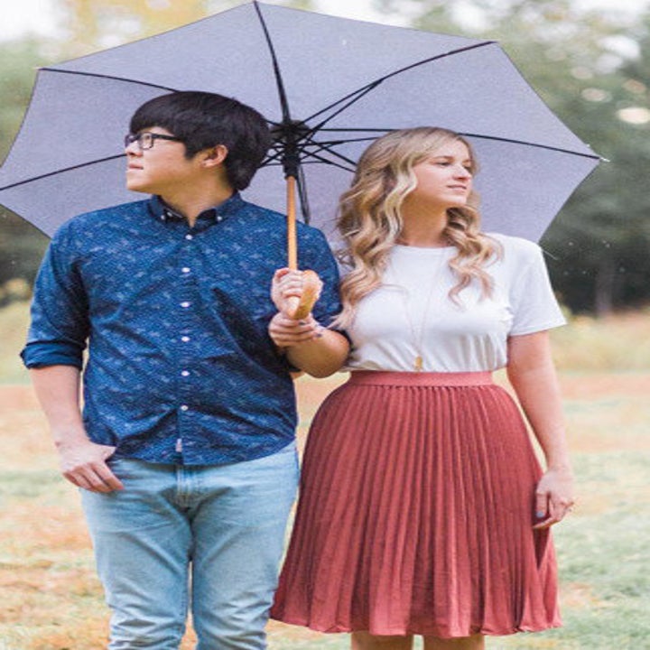 A person standing under an umbrella with their partner while wearing a tee and the skirt