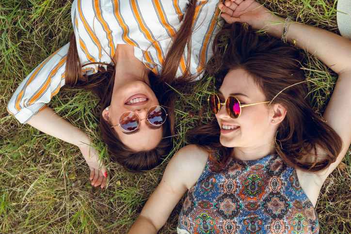 Two young people are lying down on grass in a park