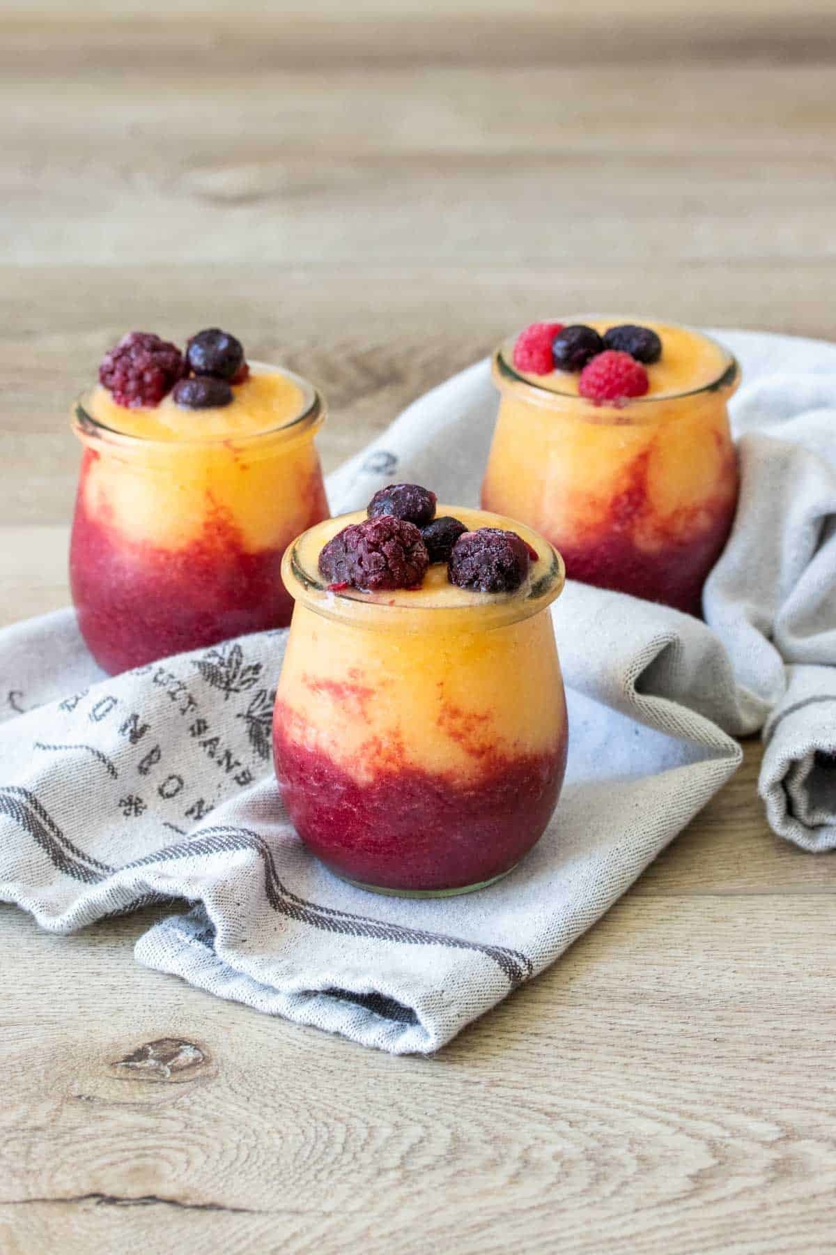 Red and orange slushies in 3 glasses topped with frozen berries. 