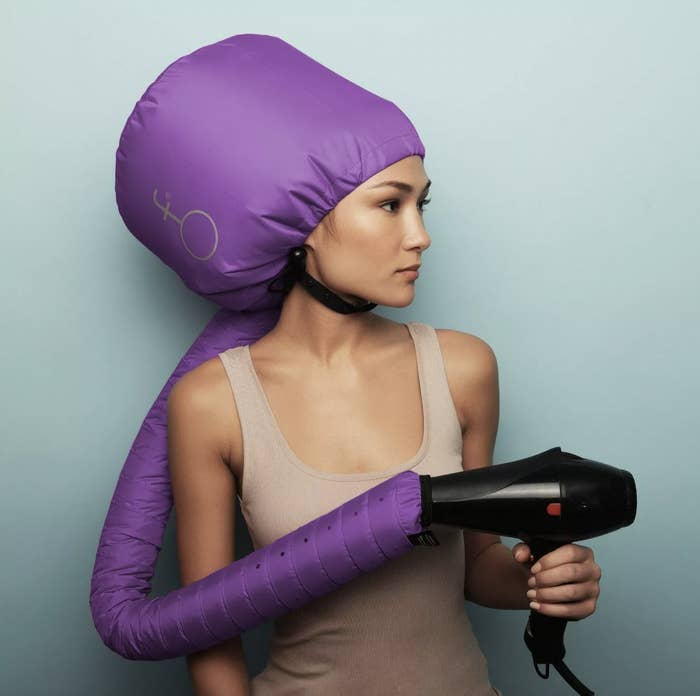 A woman wearing a hair dryer hood and hold a blow dryer