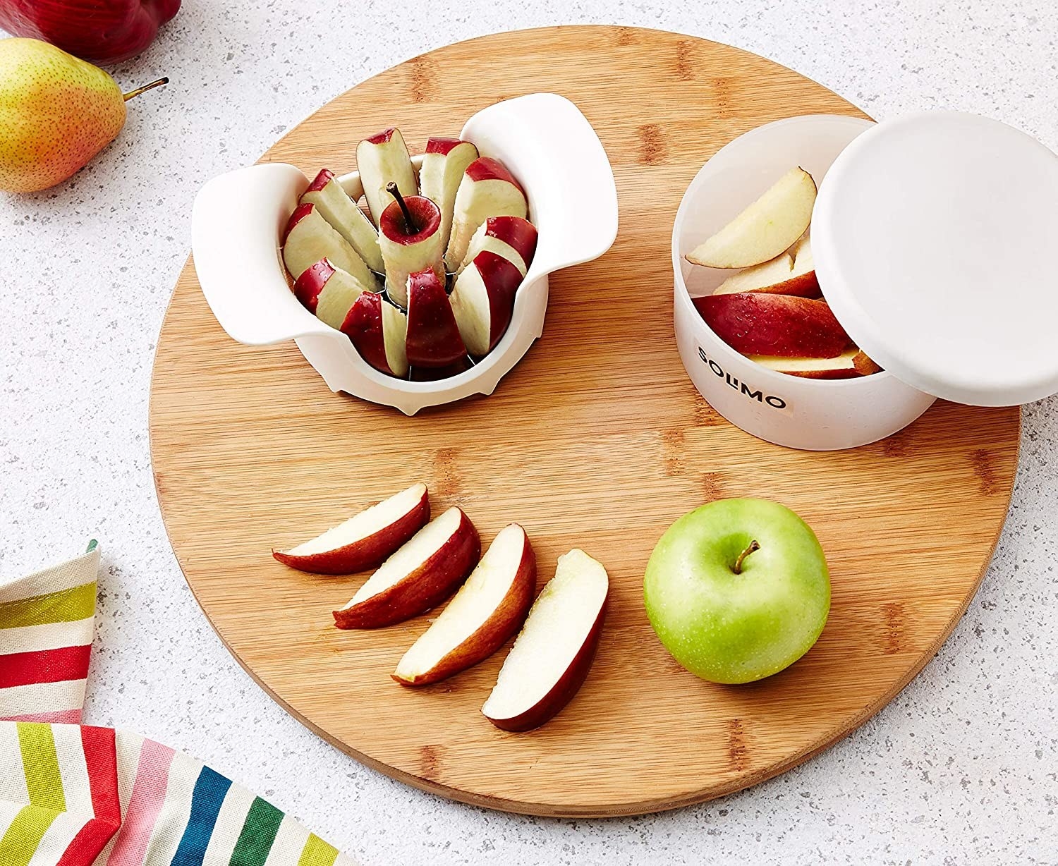 An apple cutter with apple slices and a green apple on a cutting board