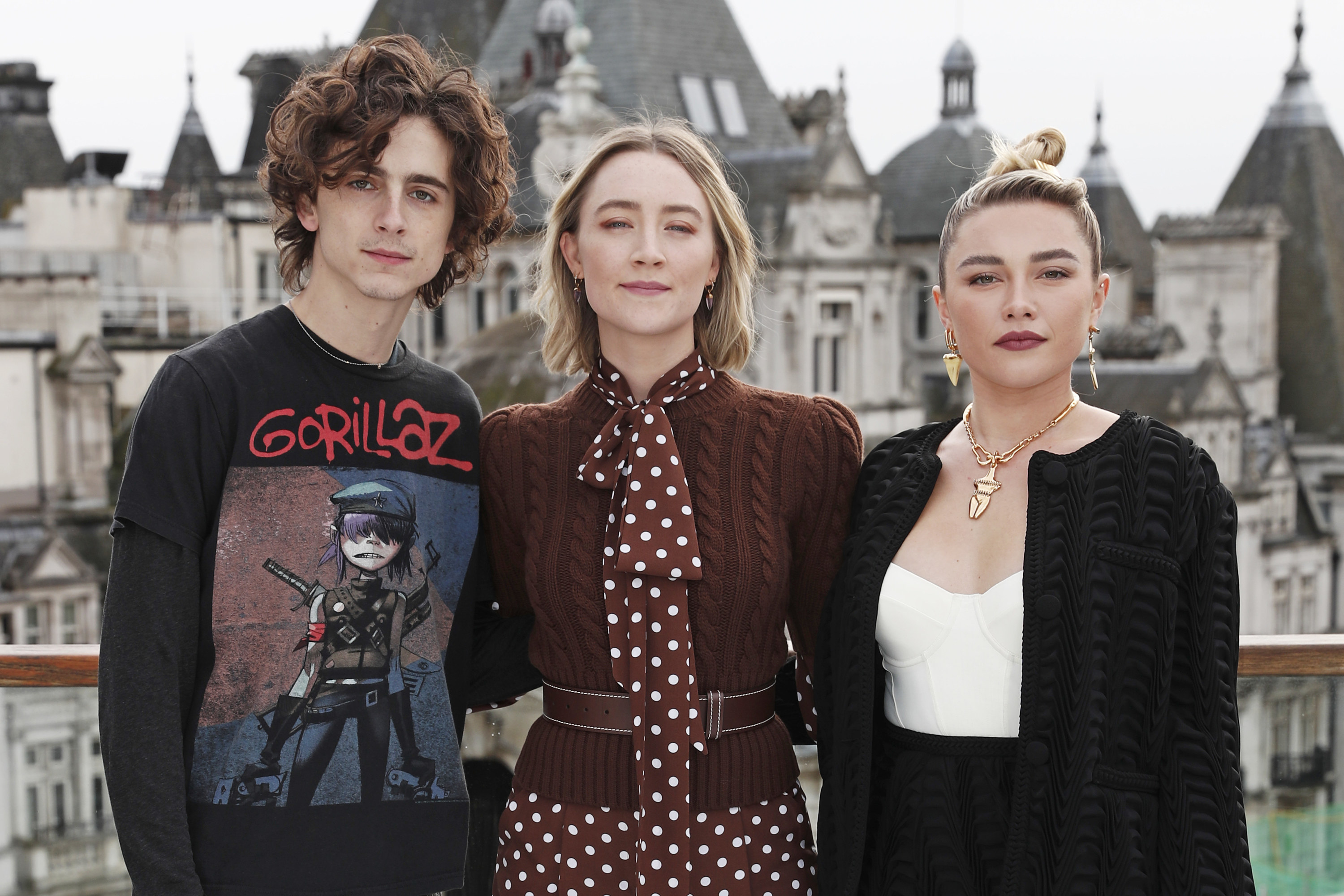 Timothée Chalamet, Saoirse Ronan, and Florence Pugh stand together against the backdrop of an elegant, castlelike building