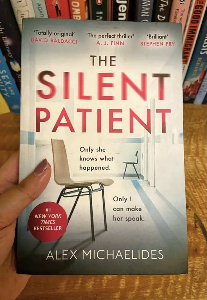 A hand holding a copy of 'The Silent Patient' by Alex Michaelides.
