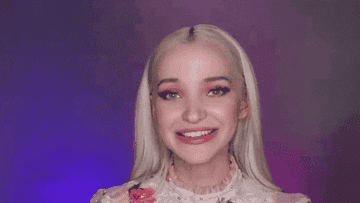 Dove Cameron giggles and looks at an iPhone in this Much gif