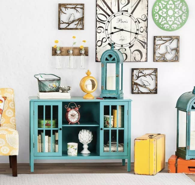 a teal storage cabinet with two glass doors and a shelf, holding decor