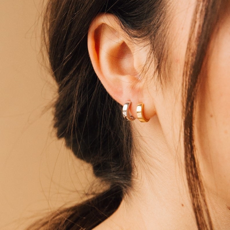 Model wearing the thick huggie hoops — one in gold and one in silver