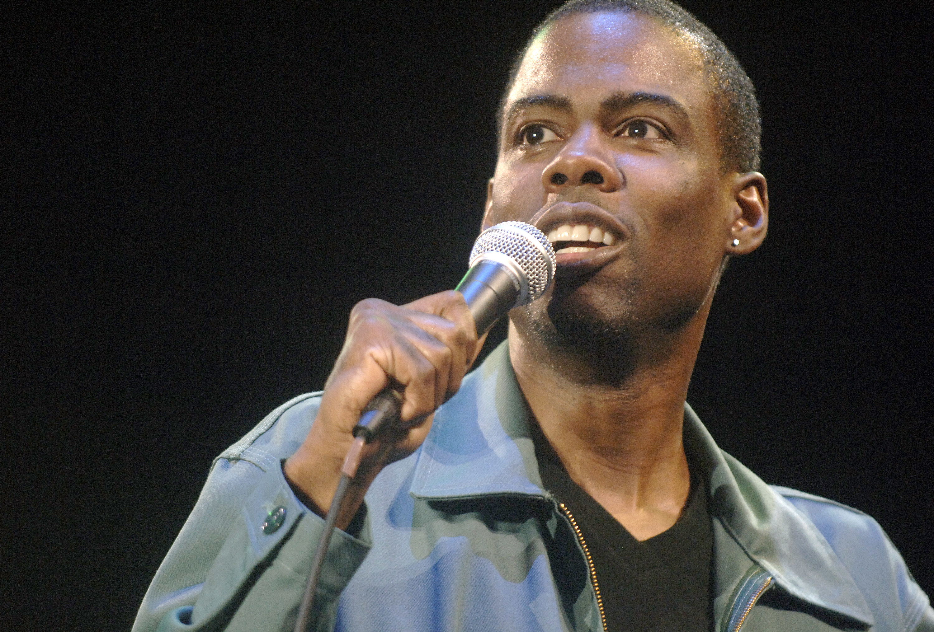 Chris Rock onstage speaks into the microphone