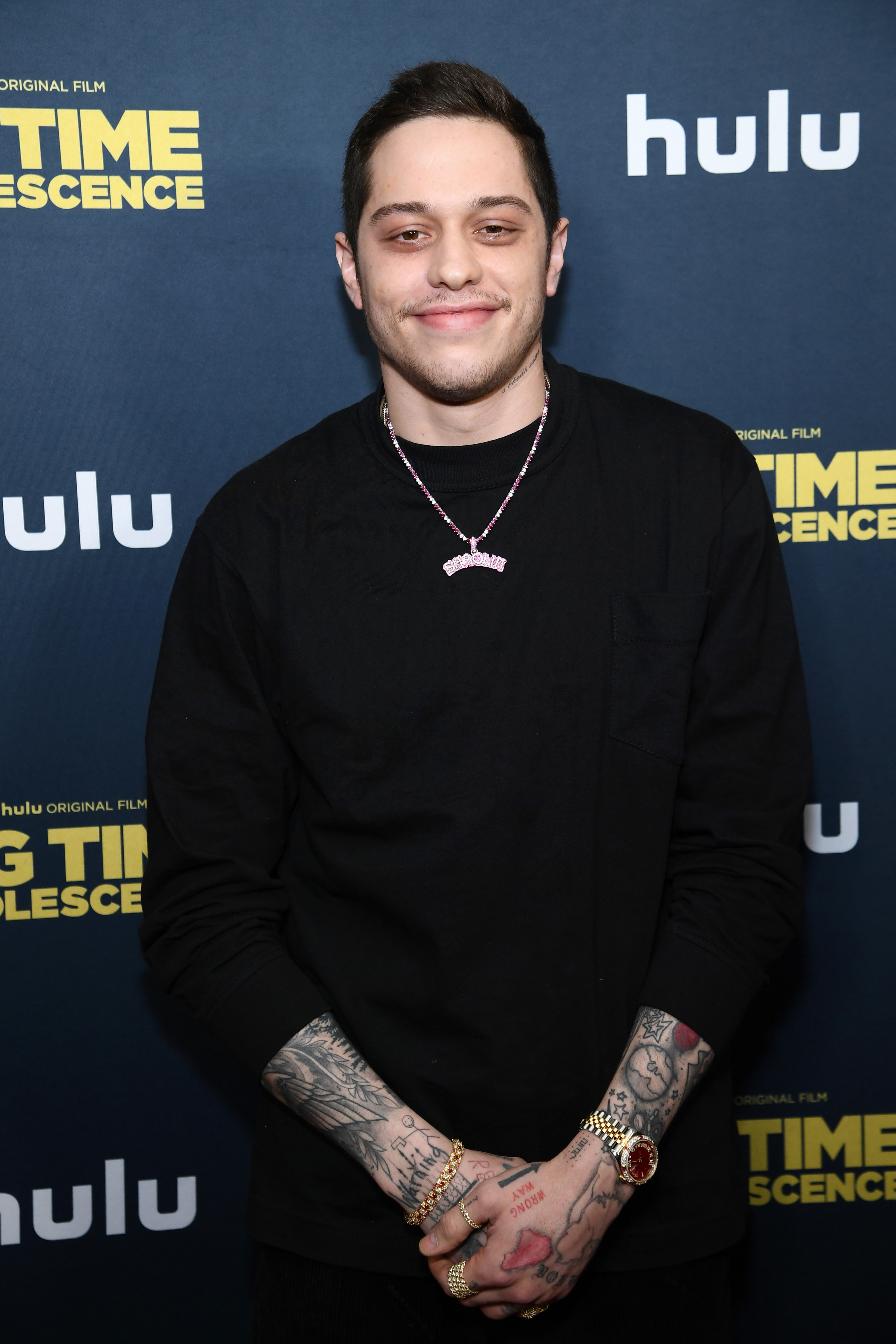 Photo of Pete Davidson at the premiere for &quot;Big Time Adolescence.&quot; He&#x27;s smiling at the camera and wearing a black sweater and a necklace that spells out &quot;SHAOLIN.&quot; The tattoos on his forearms and hands are visible.