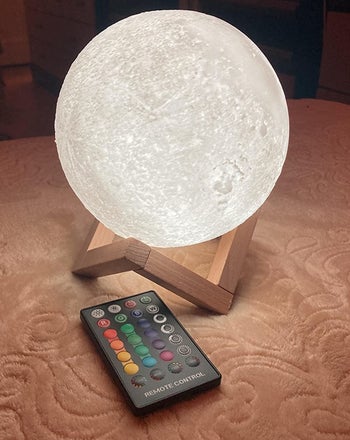 the illuminated moon lamp on a wooden base with a remote control next to it 