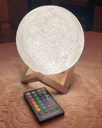 the illuminated moon lamp on a wooden base with a remote control next to it 