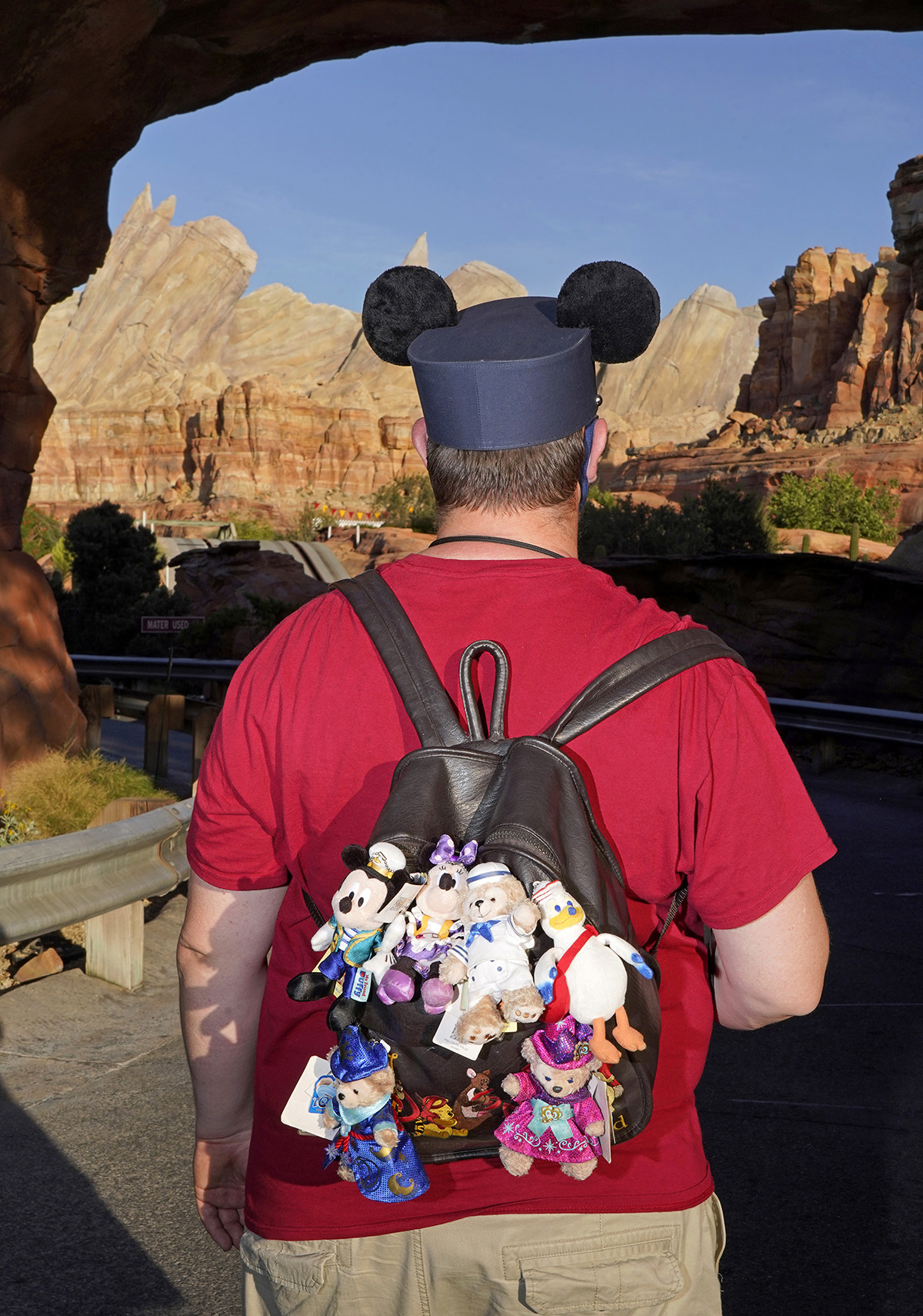 A man photographed from behind wearing Mickey ears and a backpack full of Disney keychains