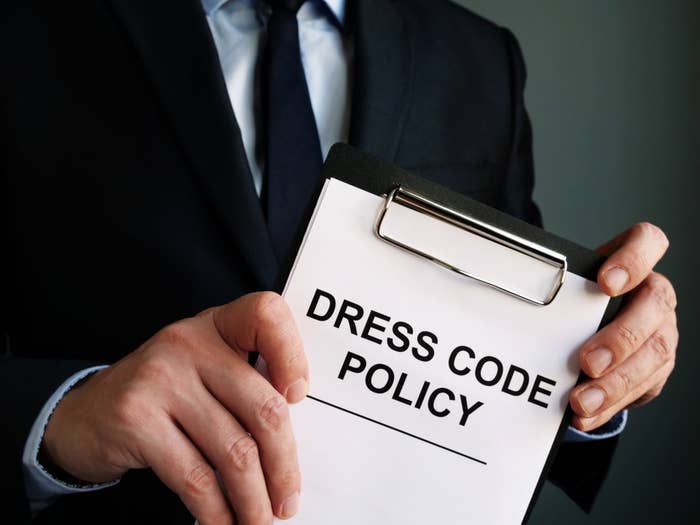 Man holding a clipboard reading, &quot;dress code policy&quot;