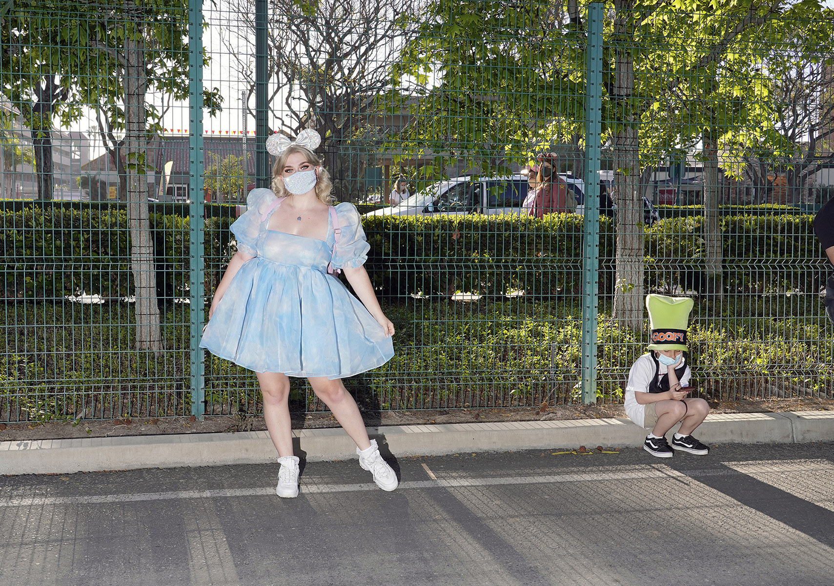 A woman in a fluffy cloud dress and bow in a park, with a young boy sitting down next to her