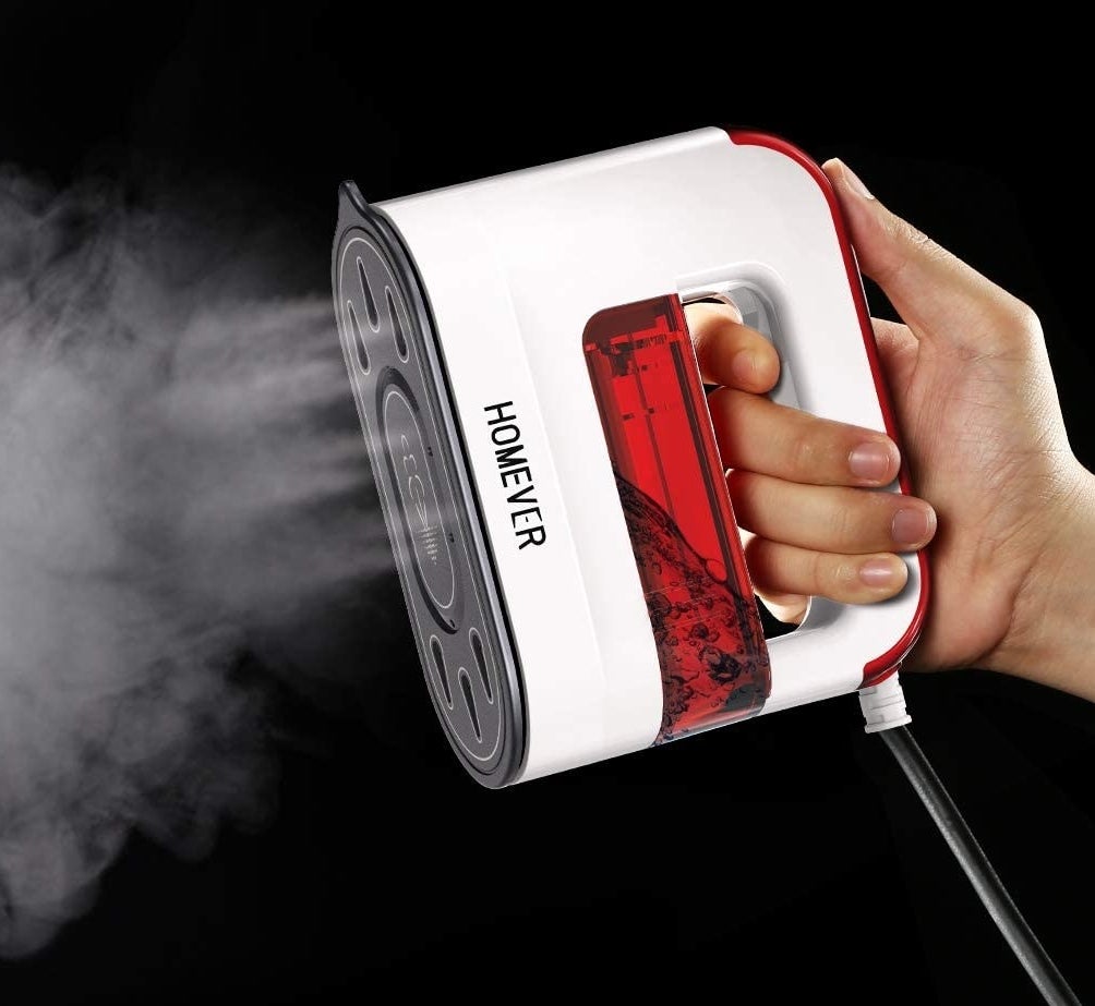 A person holding the handheld steamer while it blows out steam