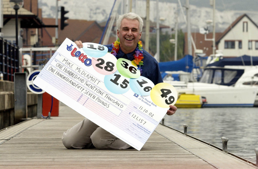 A smiling man holds giant check after winning the lotto