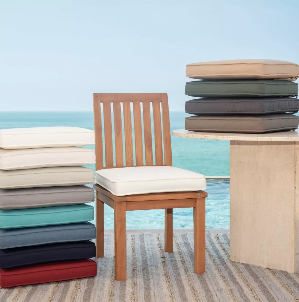 White cushion on wooden chair next to stacked cushions in various colors
