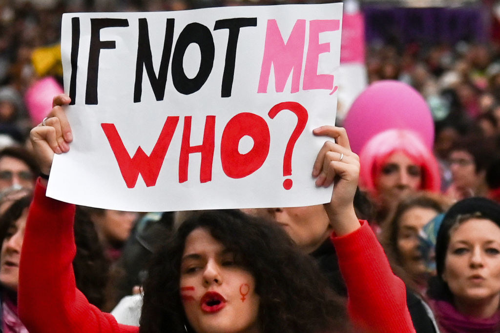 Woman holding a protest sign that says if not me, who