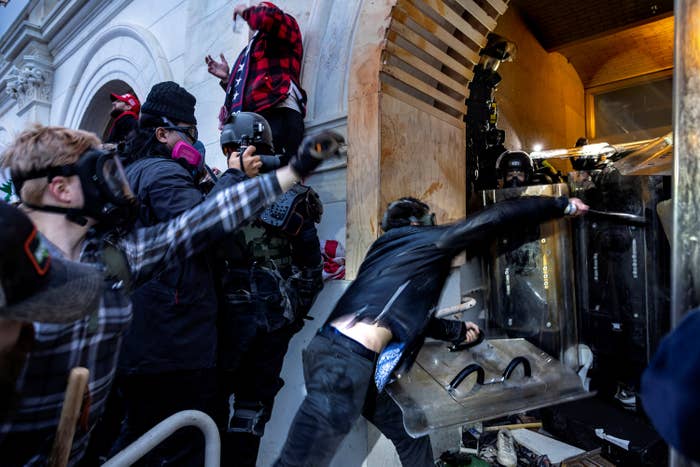 Trump supporters in riot gear try to push past a line of police holding shields blocking a door at the Capitol building