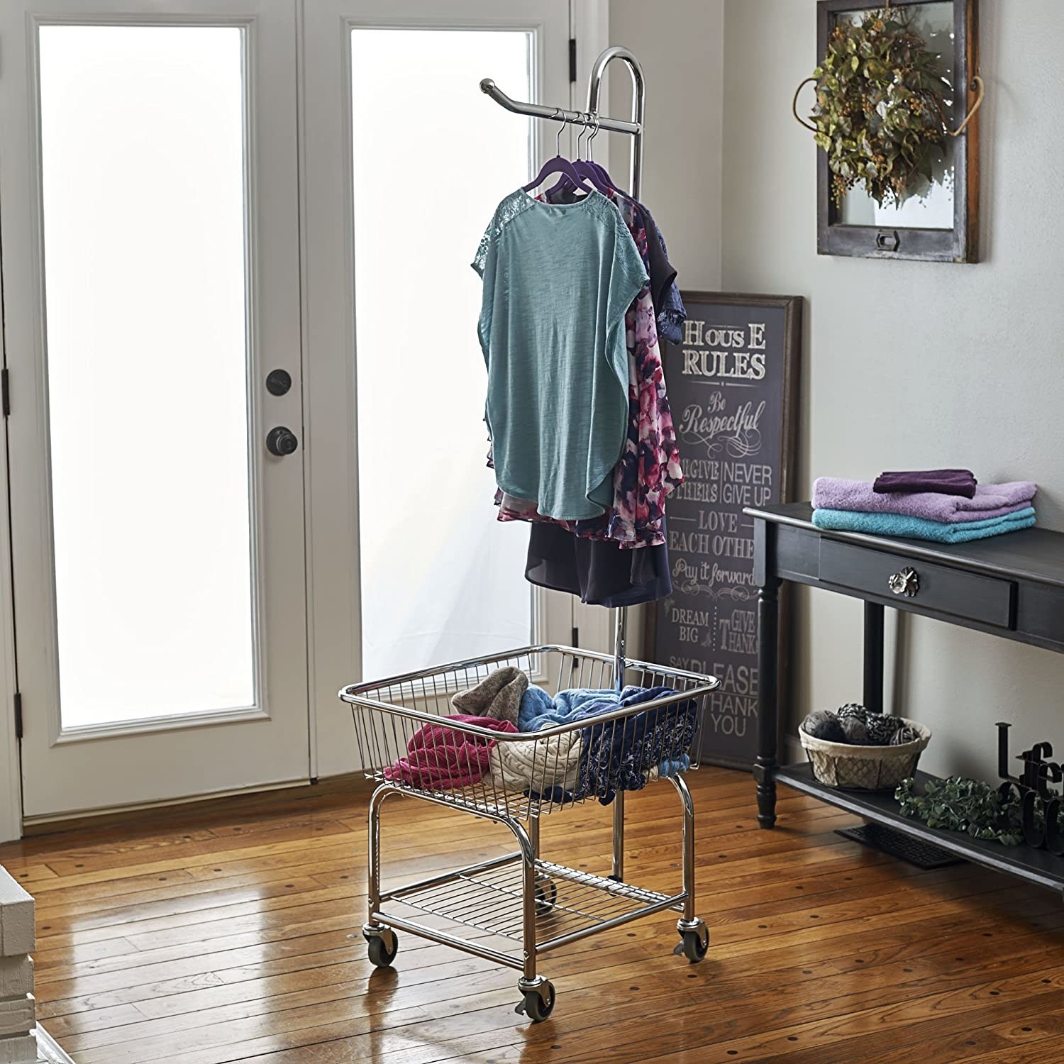 A small square laundry basket with wheels It has a tall hanging rack above it